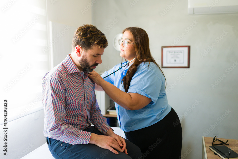 Obraz premium Female doctor listening to male patient's chest with stethoscope during medical checkup in clinic
