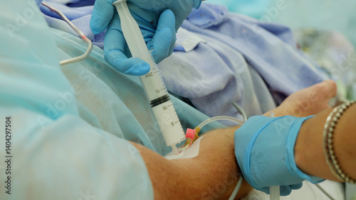 Foto Nurse wearing blue surgical gloves is injecting medicine into a catheter in a pa