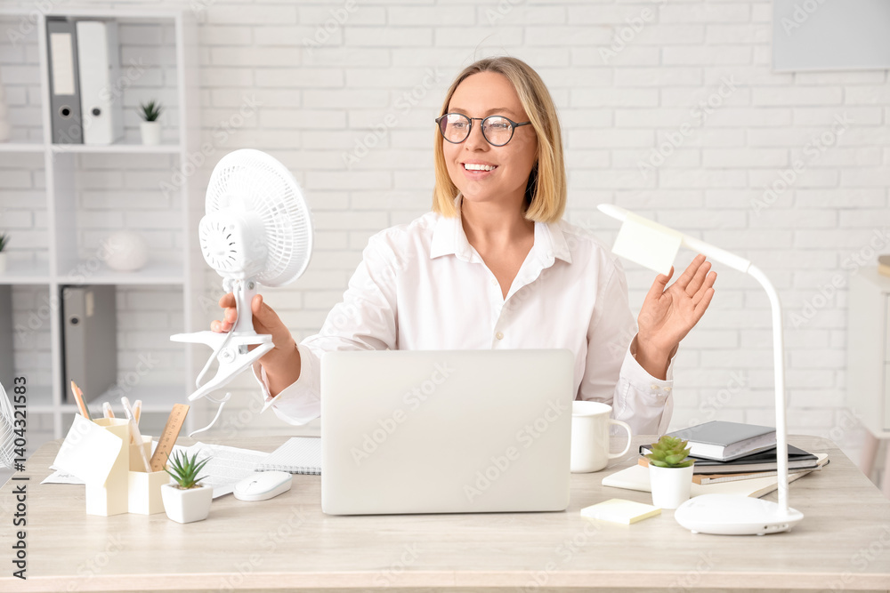 Mature happy businesswoman with electric fan and laptop in office