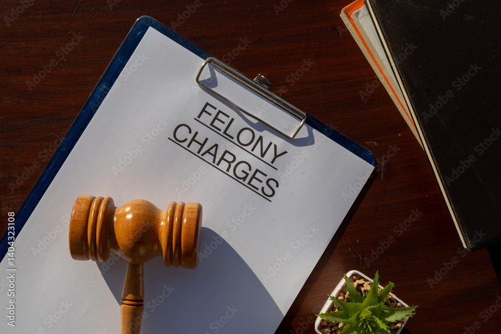 Naklejka premium A felony charges paper secured in a clipboard, placed with a gavel resting on the desk, symbolizing serious criminal offenses and judicial authority.