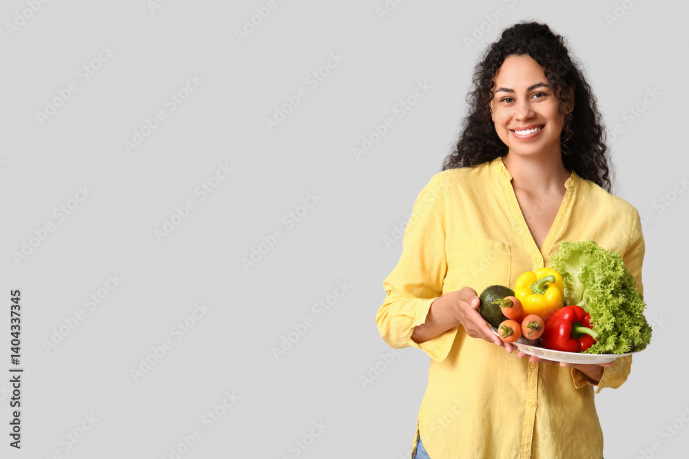 Young happy African-American woman with plate of different vegetables on grey background. Independence from Meat Day Young happy African-American woman with plate of different vegetables on grey background. Independence from Meat Day