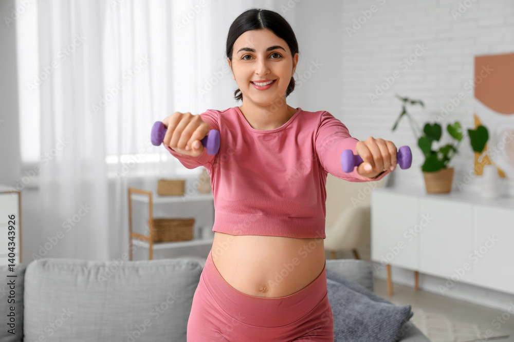 Beautiful pregnant woman training with dumbbells in living room