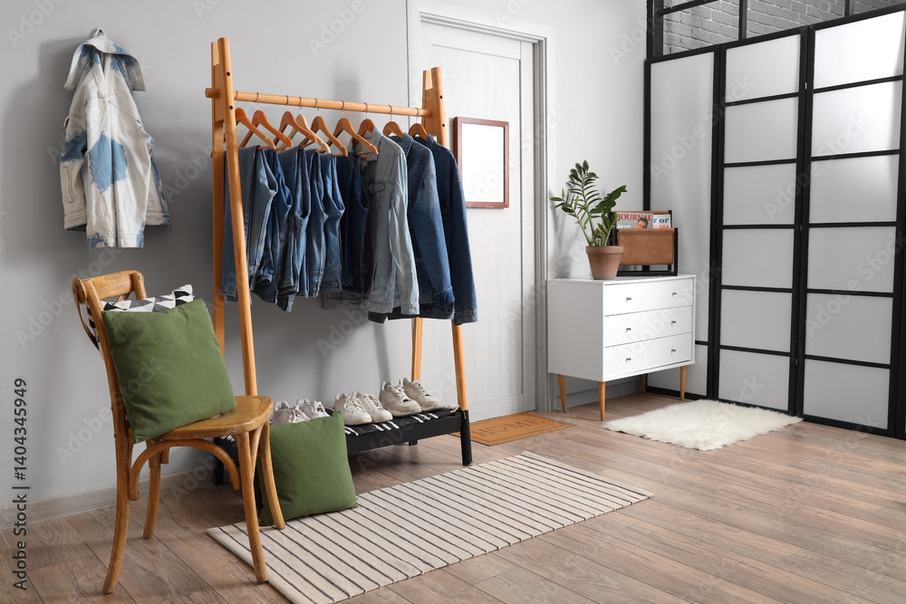 Rack with stylish denim clothes near white wall in room