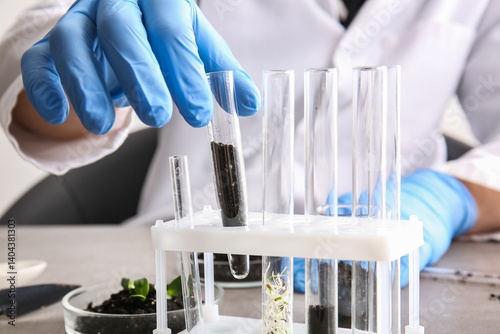 Scientist working with soil sample and plant seedlings in laboratory, closeup