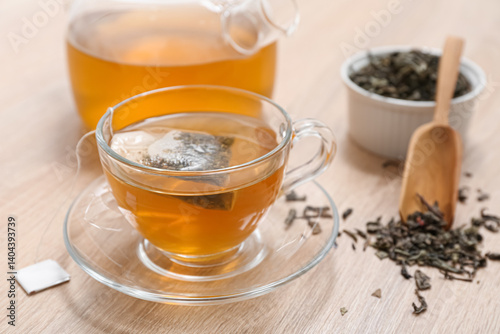 Glass cup of hot green tea and dried leaves on wooden background