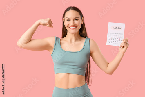 Sporty young woman with menstrual calendar showing muscles on pink background
