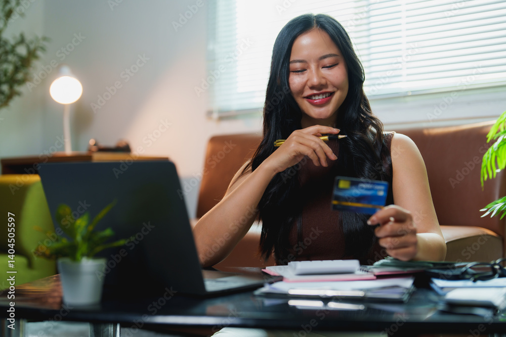 Young asian woman holding credit card and using laptop computer buying online, smiling female paying with credit card on internet banking, cheerful girl using computer for online shopping at home