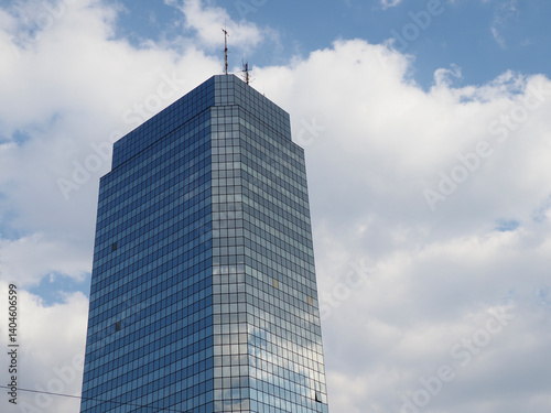 Modern Glass Skyscraper with Reflective Facade Against Blue Sky with White Clouds