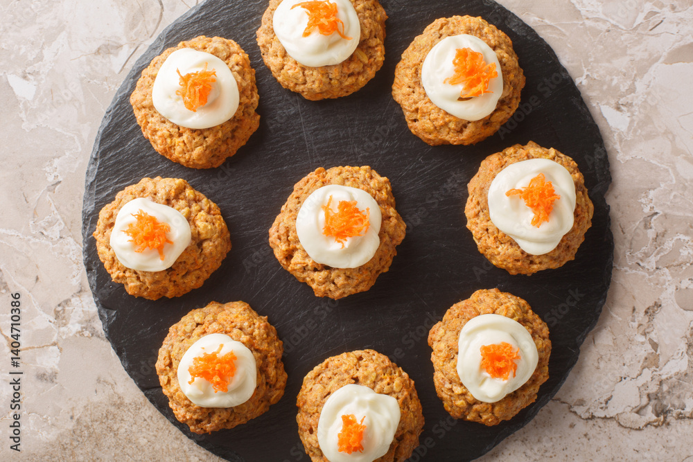Soft crumbly carrot oatmeal cookie cake with cream cheese frosting close-up on plate on table. Horizontal top view from above
