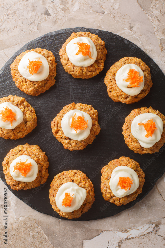 Delicious carrot cake cookies with cream cheese frosting are a must-have Easter dessert close up on the plate on the table. Vertical top view from above