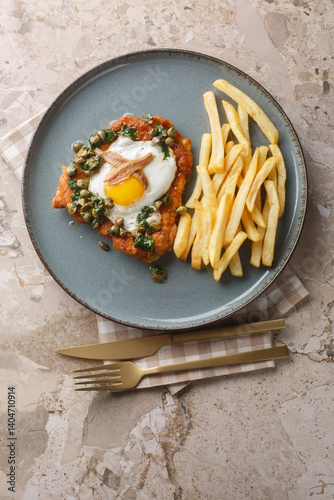 Obraz na płótnie German Schnitzel holstein serve with a fried egg, anchovy and lemony caper sauce close up on the plate on the table. Vertical top view from above w salonie