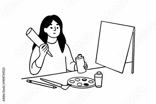 Picture of serious concentrated young Caucasian female artist sitting at desk with painting accessories, holding tube of oil paint, mixing colors on palette; unfinished painting on canvas near her