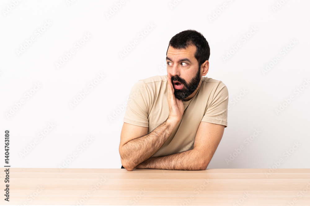 Caucasian man with beard in a table whispering something with surprise gesture while looking to the side. Caucasian man with beard in a table whispering something with surprise gesture while looking to the side.