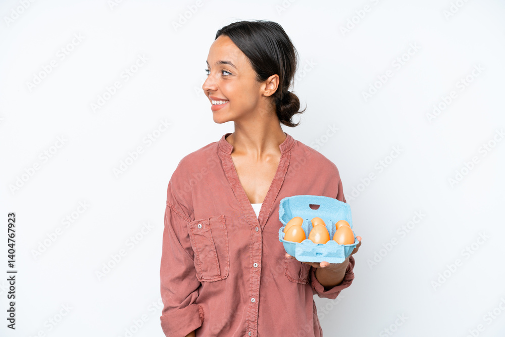 Young hispanic woman holding eggs isolated on white background looking to the side and smiling Young hispanic woman holding eggs isolated on white background looking to the side and smiling