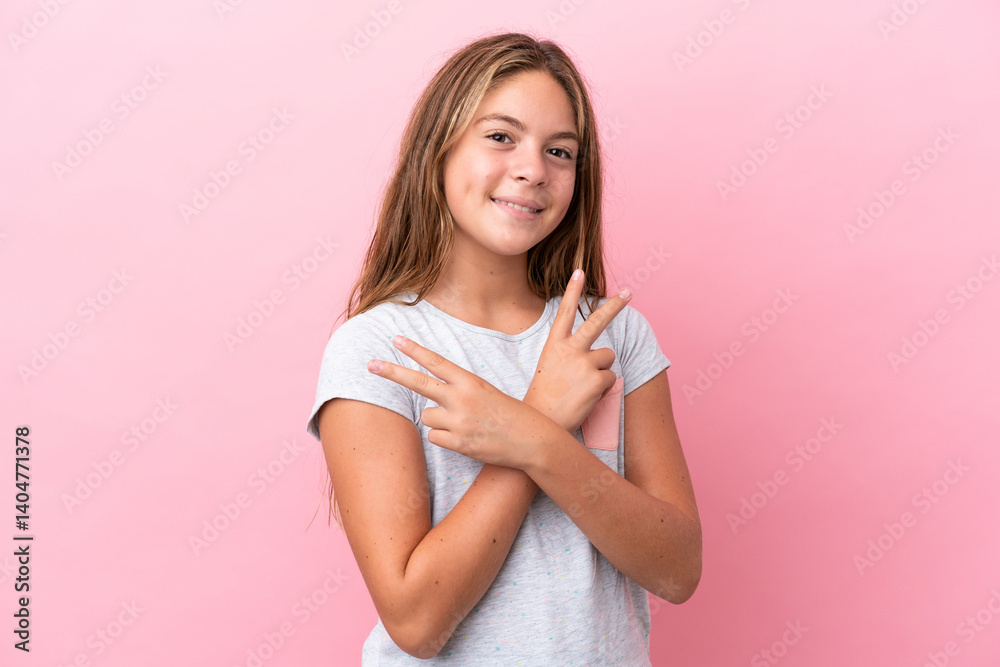 Little caucasian girl isolated on pink background smiling and showing victory sign