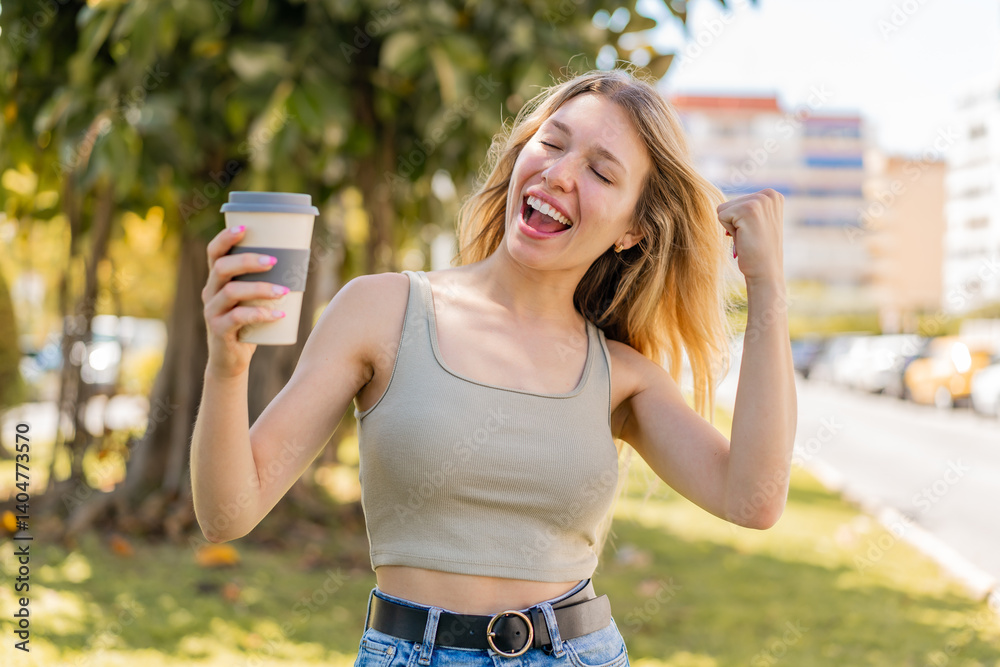 Young blonde woman holding a take away coffee at outdoors celebrating a victory Young blonde woman holding a take away coffee at outdoors celebrating a victory
