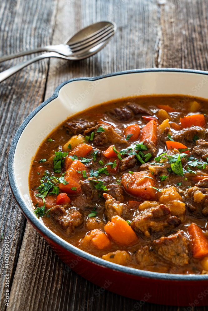 Beef goulash with vegetables in frying pan on wooden table Beef goulash with vegetables in frying pan on wooden table