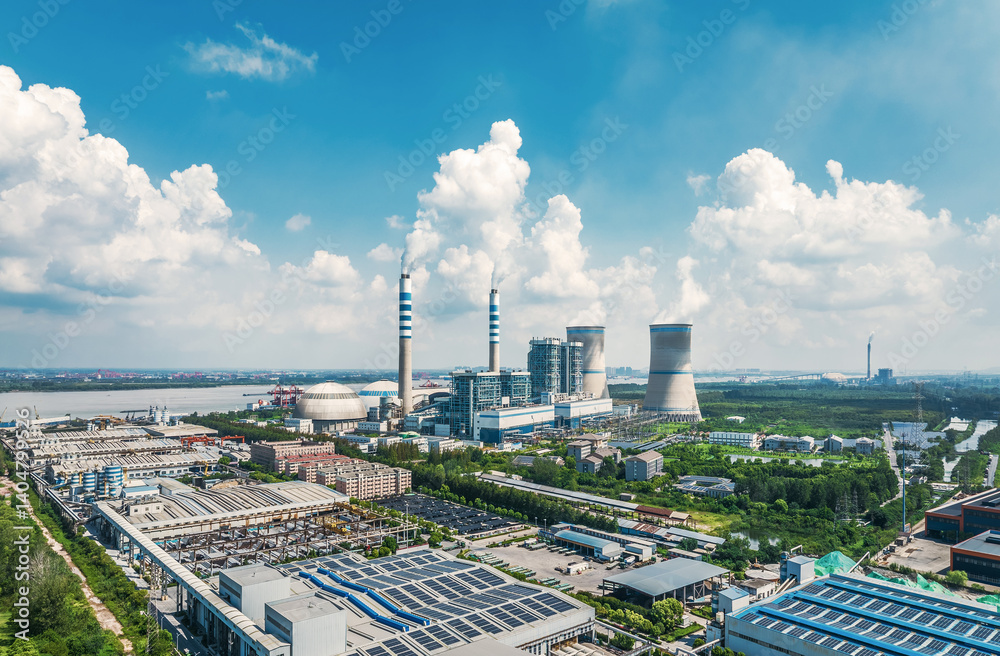 Obraz premium Aerial view of a large power plant complex with cooling towers chimneys solar panels near a river.