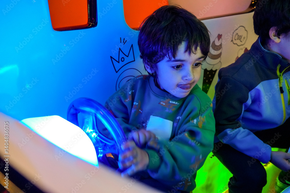 Child driving toy car in amusement park with neon lights