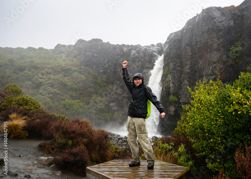 Obraz na płótnie Tourist posing for fun photos at Taranaki Falls in the rain. Tongariro National Park. New Zealand. w salonie