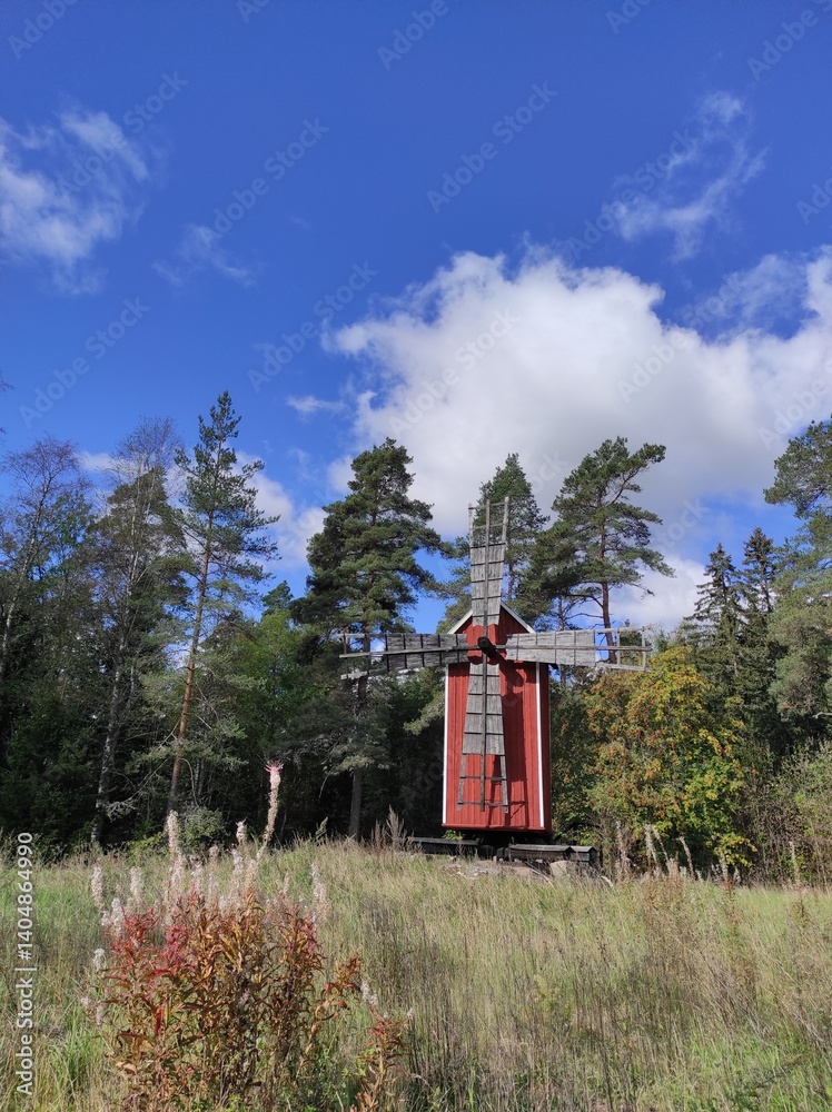 Windmill in the summer forest against the blue sky with clouds