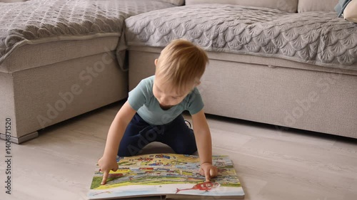 Curious toddler sitting on floor and exploring colorful picture book


