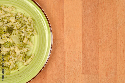 A light green plate contains a serving of pasta with broccoli, set on a wooden table