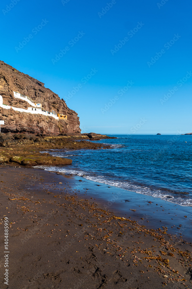 Tufia village on gran canaria island with black sand beach and blue sea waves crashing on the shore