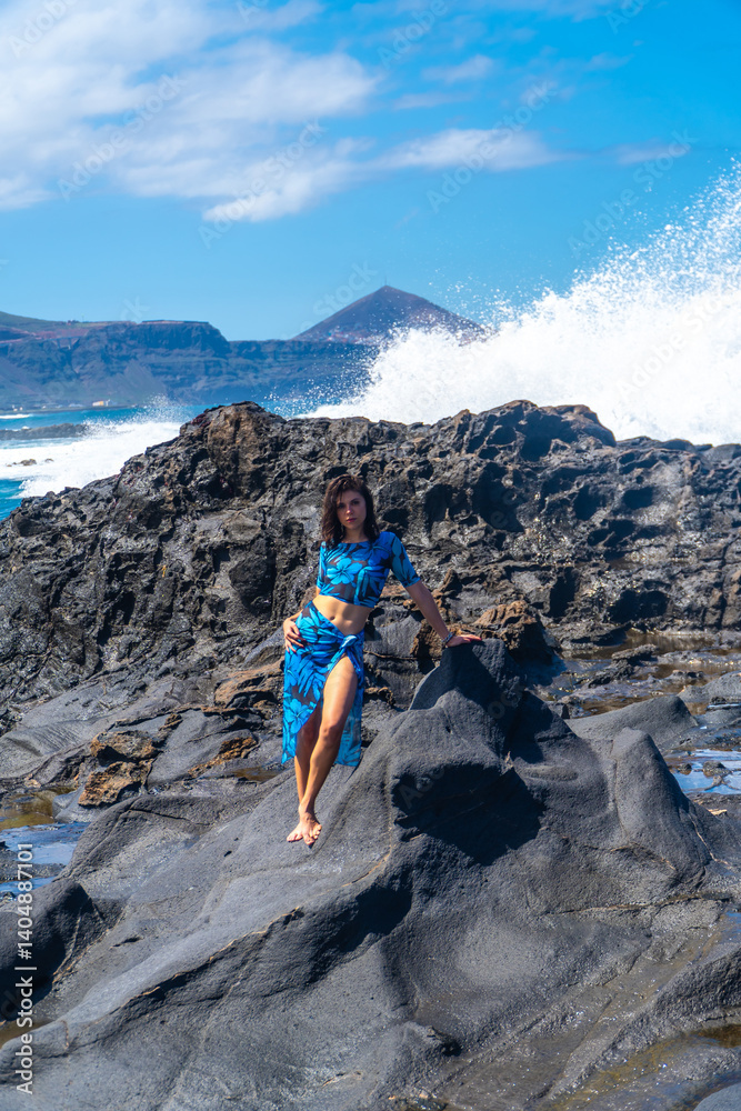 Young woman posing on volcanic rocks with ocean waves crashing in gran canaria, spain