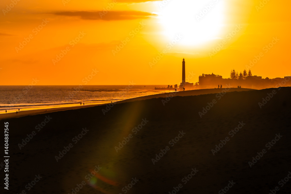 Tourists walking on maspalomas dunes at sunset with lighthouse in background