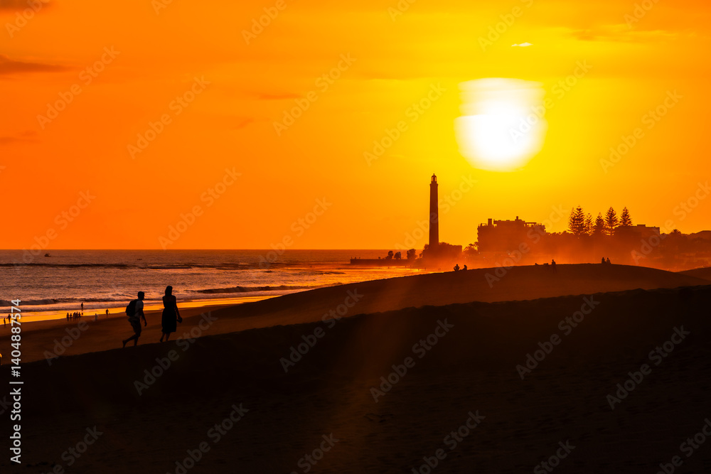 Tourists walking on maspalomas dunes at sunset with lighthouse in background