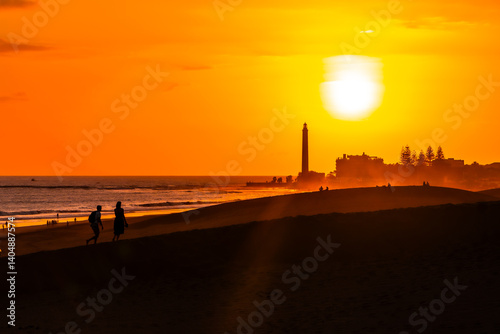 Obraz na płótnie Tourists walking on maspalomas dunes at sunset with lighthouse in background w salonie