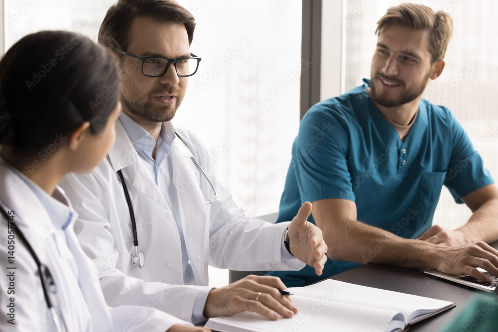 Fototapeta premium Collaboration in medicine. Confident young male head doctor lead round table briefing with diverse team of medical professionals discuss patients cases based on paper register offer treatment strategy