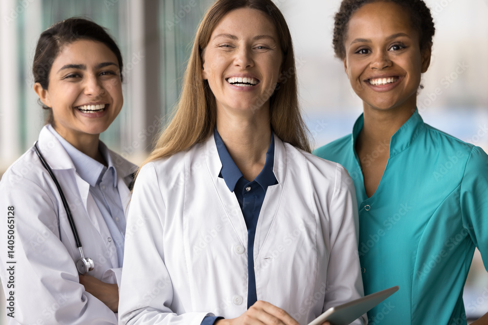 Fototapeta premium Successful medical professionals. Group portrait three happy smiling confident beautiful young women doctors of different ethnicities specialties pose together look at camera enjoy teamwork in clinic