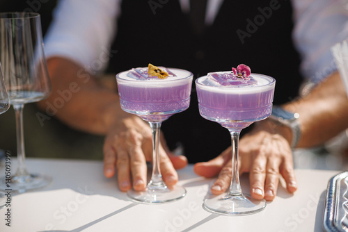 A skilled bartender is meticulously preparing two vibrant purple cocktails on a beautifully arranged table, contributing to the ambiance of the setting