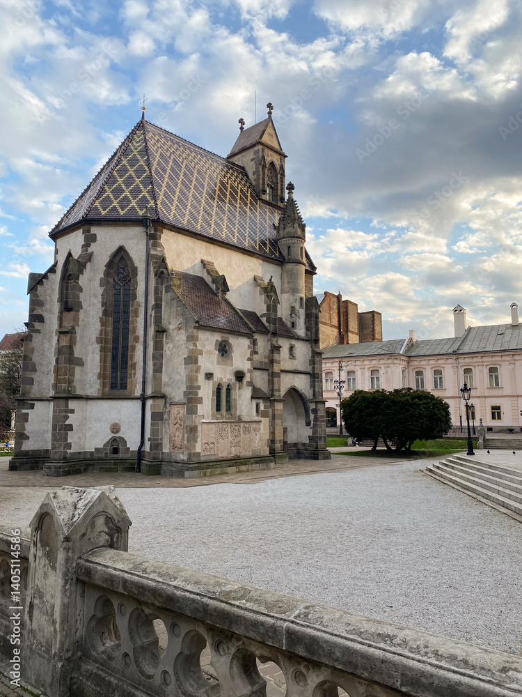 Obraz premium A historic church with a distinctive tiled roof, surrounded by a quiet plaza.