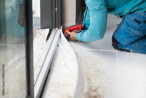 Construction worker installing thermal insulation around window using nail gun