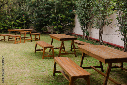 Canvas Print Outdoor picnic area with wooden tables and benches on a lush green lawn, perfect for gatherings and relaxation in a natural setting