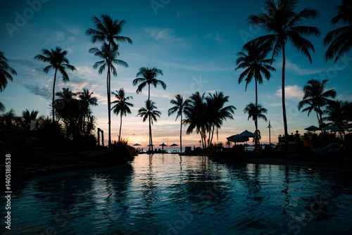 Obraz na płótnie A tropical beach at twilight in Thailand, featuring silhouettes of palm trees and shimmering reflections on the water, exuding luxury and tranquility. w salonie