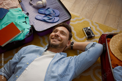 Young man lying on floor dreaming about future vacation trip