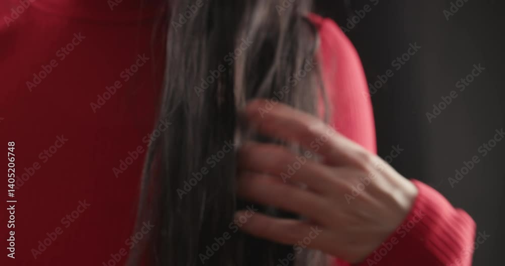 Brunette woman in red clothes smoothly runs her fingers through her wavy hair, creating a hypnotizing effect on an isolated black background