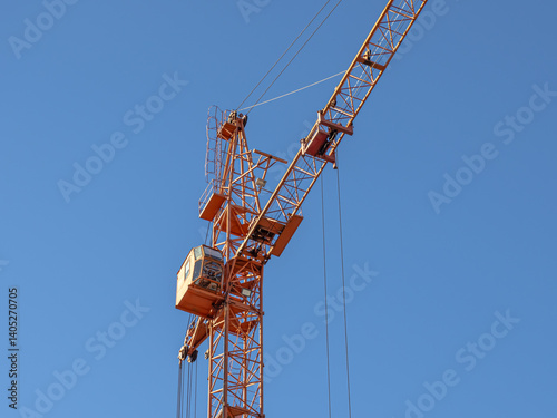 Equipment for the construction and lifting of bulky goods with construction materials. A tower crane on a construction site against a blue sky background. Construction equipment.