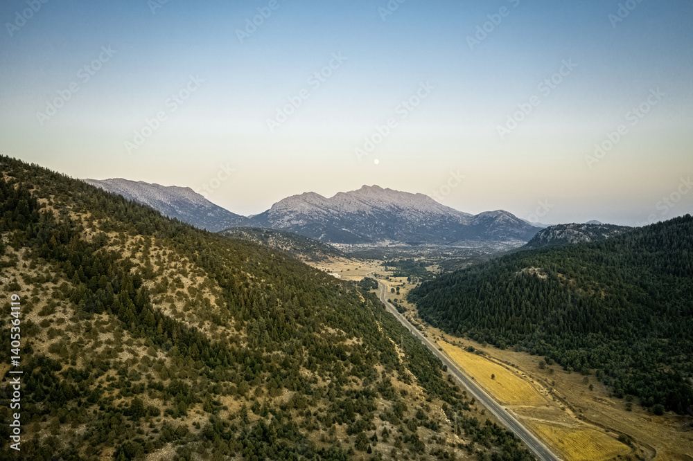Winding asphalt mountain road with green forest lined with trees on both sides under cloudy sky. Drone footage.