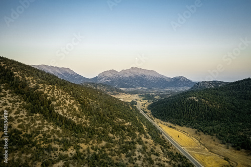 Obraz na płótnie Winding asphalt mountain road with green forest lined with trees on both sides under cloudy sky. Drone footage. w salonie