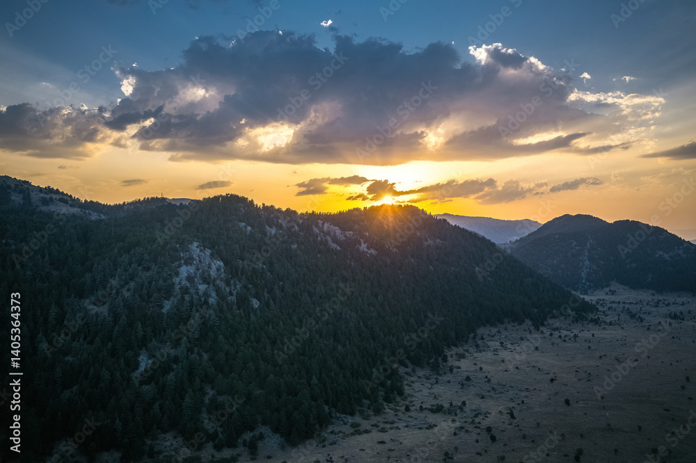 Dramatic skies created by the sunrise in the early morning hours and the yellow sunbeams filtering through the clouds towards the mountains.