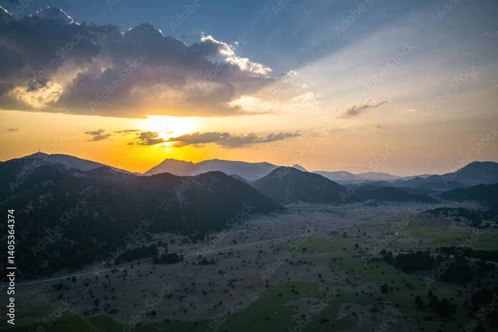 Dramatic skies created by the sunrise in the early morning hours and the yellow sunbeams filtering through the clouds towards the mountains.