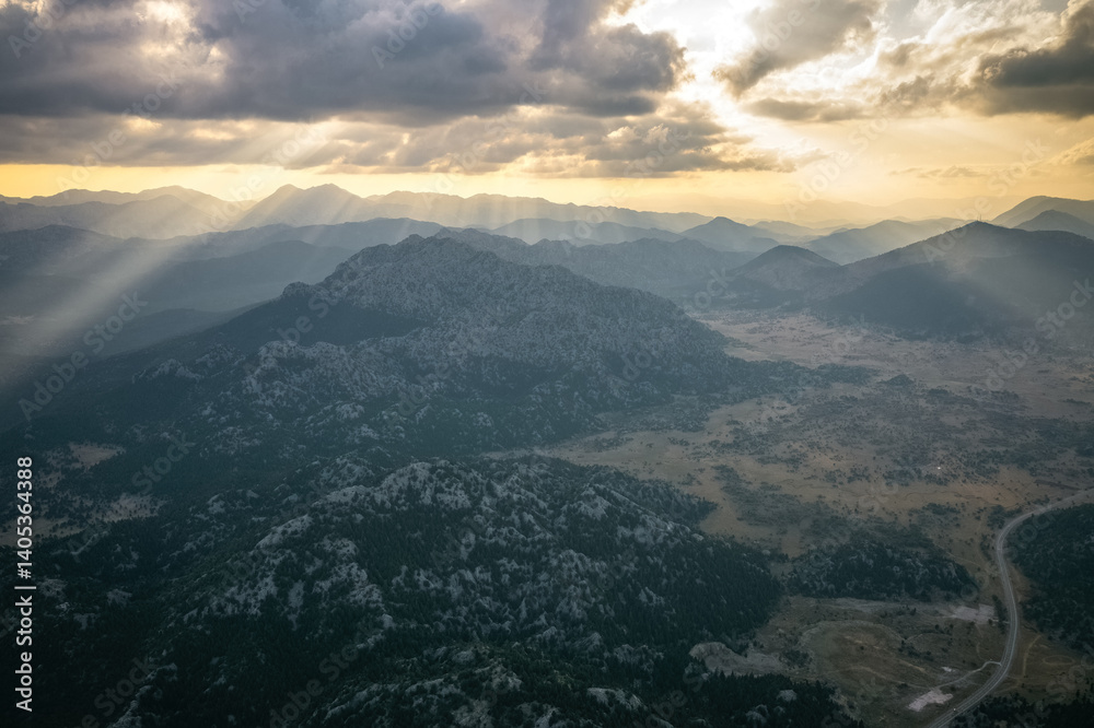 An impressive sunrise skyscape in the early morning. Yellow sun rays filter through the clouds towards the mountains and the ground.