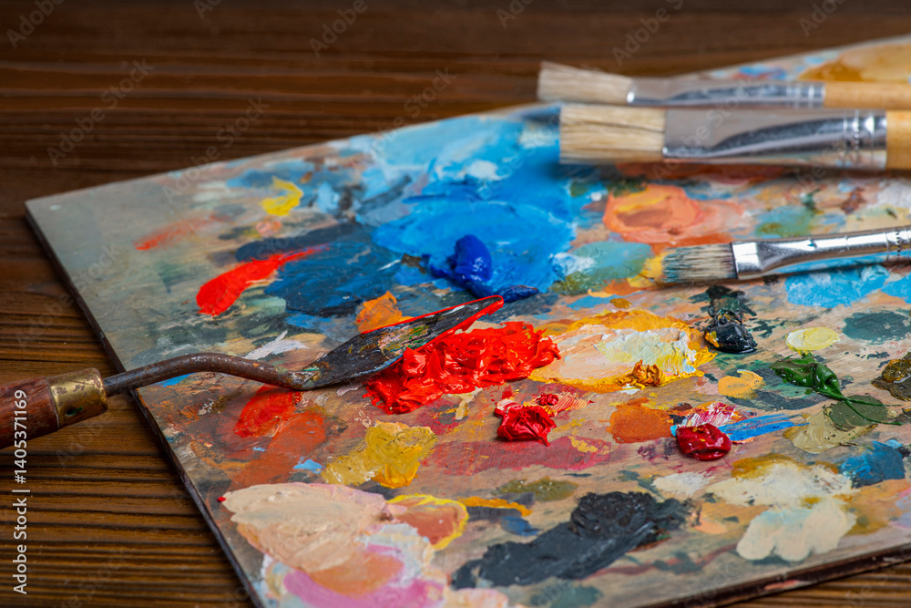 Old used brushes and palette knife in an artist's studio, palette with multi-colored spots of oil or acrylic paint Old used brushes and palette knife in an artist's studio, palette with multi-colored spots of oil or acrylic paint