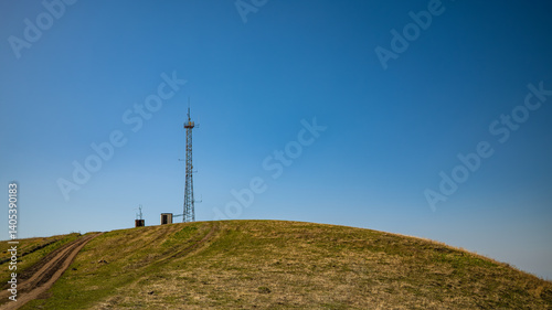 Telecommunications tower on hilltop with equipment cabins against clear blue sky