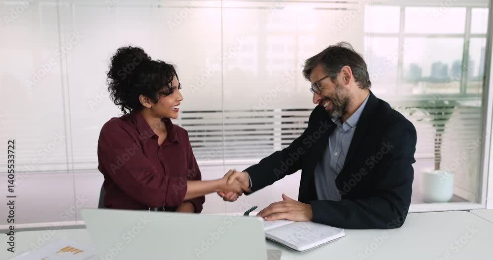 Smiling Indian businesswoman shaking hands with businessman seated at meeting table, closing commercial deal, start partnership, concluding successful job interview or negotiation. Business, etiquette Smiling Indian businesswoman shaking hands with businessman seated at meeting table, closing commercial deal, start partnership, concluding successful job interview or negotiation. Business, etiquette